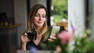 Frau sitzt beim Kaffee mit Smartphone in der Hand